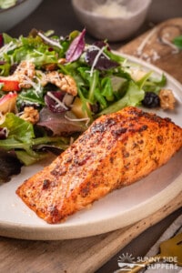 A salmon fillet served with a side of green salad on a white stoneware plate.